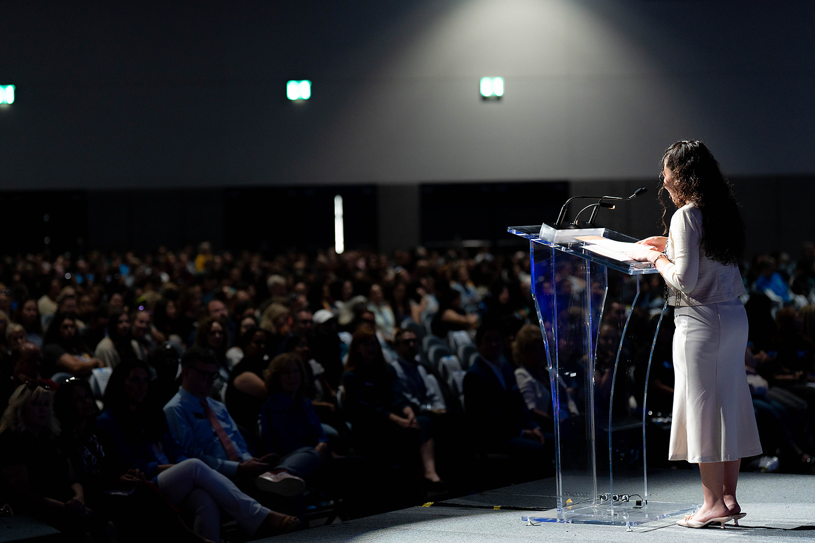 A person in white attire speaking at a transparent podium in front of a large audience