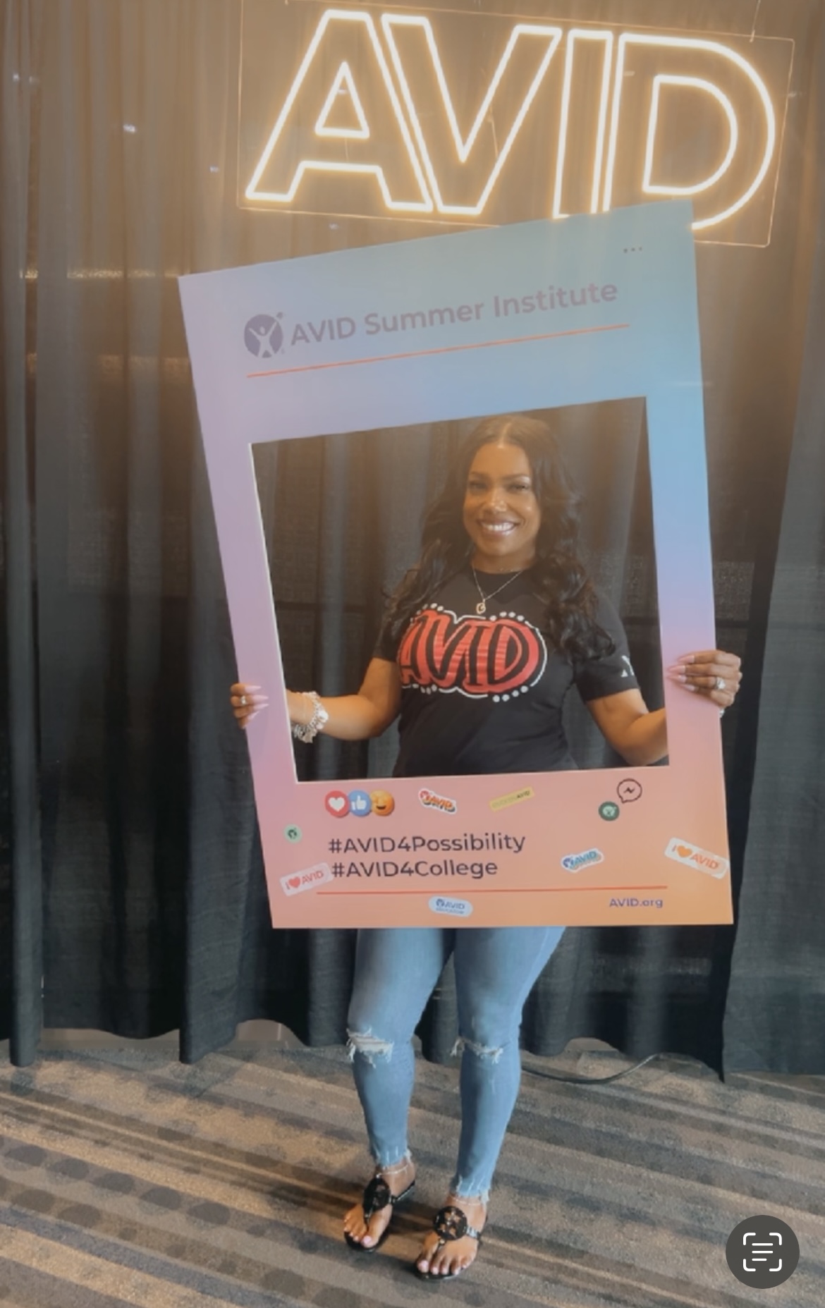 Individual holding a frame with AVID Summer Institute branding, in front of an AVID sign.