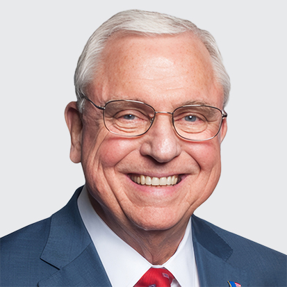 An individual with grey hair wearing a blue suit jacket and a red tie.