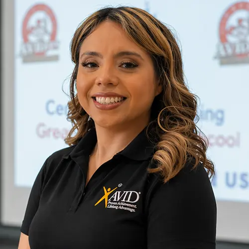 Individual with blurred face wearing a black AVID polo shirt standing indoors with a presentation in the background. Individual with blurred face wearing a black AVID polo shirt standing indoors with a presentation in the background.
