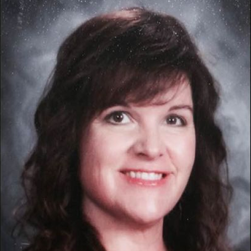 A portrait with long, dark curly hair against a grey background. The face is pixelated for privacy.
