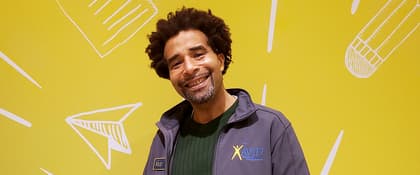 A person wearing a grey jacket with a yellow background displaying an AVID logo and various white line drawings. A person wearing a grey jacket with a yellow background displaying an AVID logo and various white line drawings.