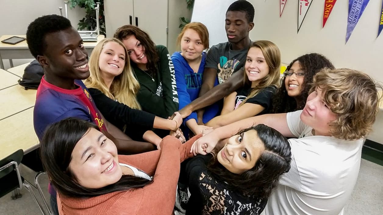 A group of people standing in a classroom, forming a human circle by holding hands. A group of people standing in a classroom, forming a human circle by holding hands.