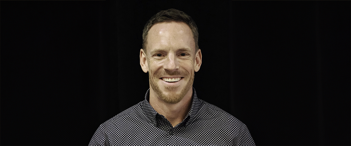 A person wearing a patterned shirt against a dark background with their head centered in the image.