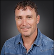 Image of a person wearing a collared denim shirt posed against a dark background.
