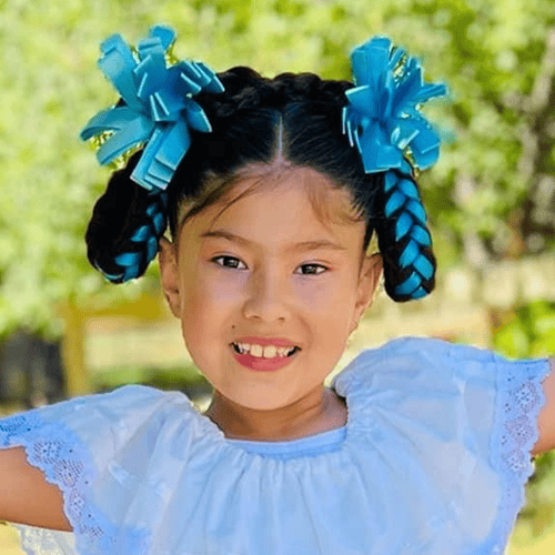 Person with black braided hair adorned with blue ribbon bows, wearing a light blue dress with lace trim. Person with black braided hair adorned with blue ribbon bows, wearing a light blue dress with lace trim.