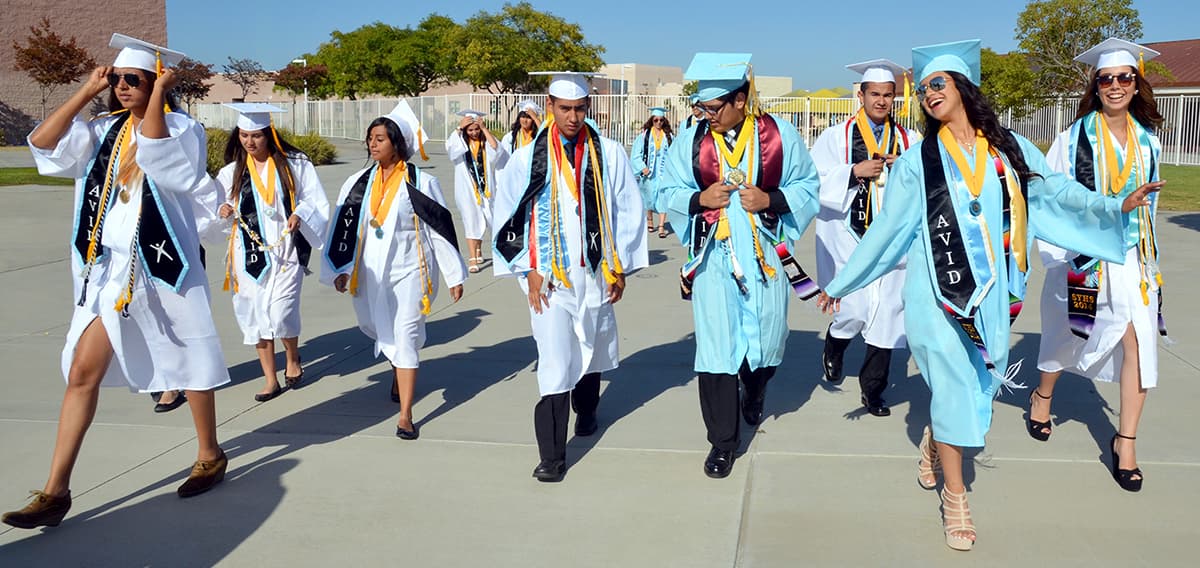 A group of graduates in caps and gowns walking outside on a sunny day. A group of graduates in caps and gowns walking outside on a sunny day.