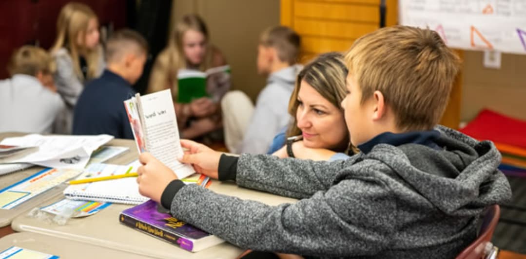 Image of students reading books and studying at a table in a classroom setting. Image of students reading books and studying at a table in a classroom setting.