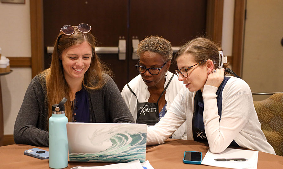 Three individuals sitting at a table, engaging in a discussion around a laptop with ocean wave design.