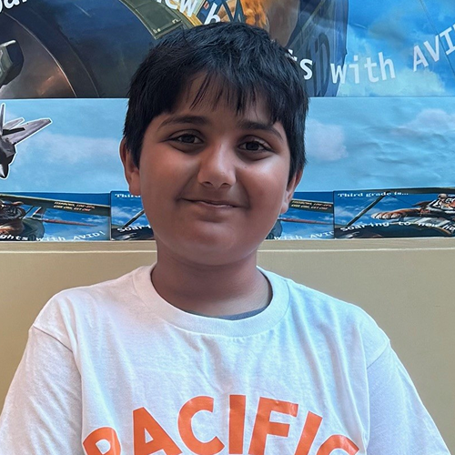 A person wearing a white t-shirt with orange lettering, standing in front of a colorful background featuring aircraft.