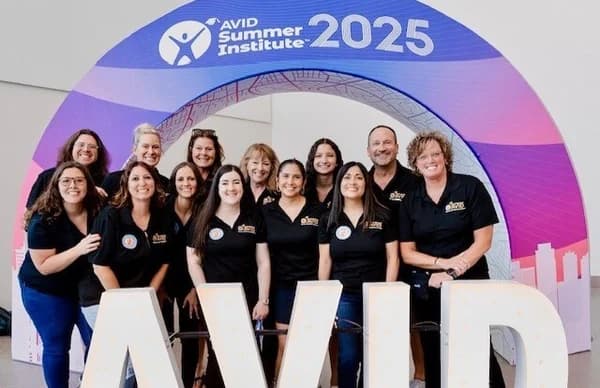 Group of people wearing matching black AVID shirts standing together under a sign that reads 'AVID Summer Institute 2025'. Group of people wearing matching black AVID shirts standing together under a sign that reads 'AVID Summer Institute 2025'.