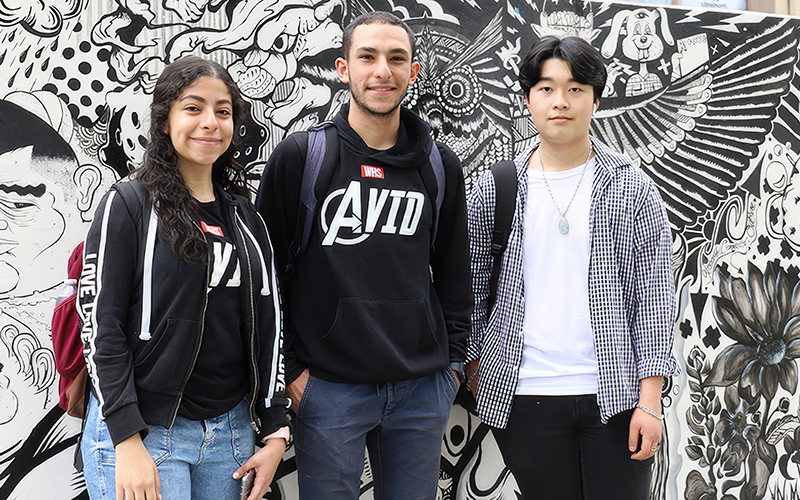 Three people standing in front of a black and white mural.