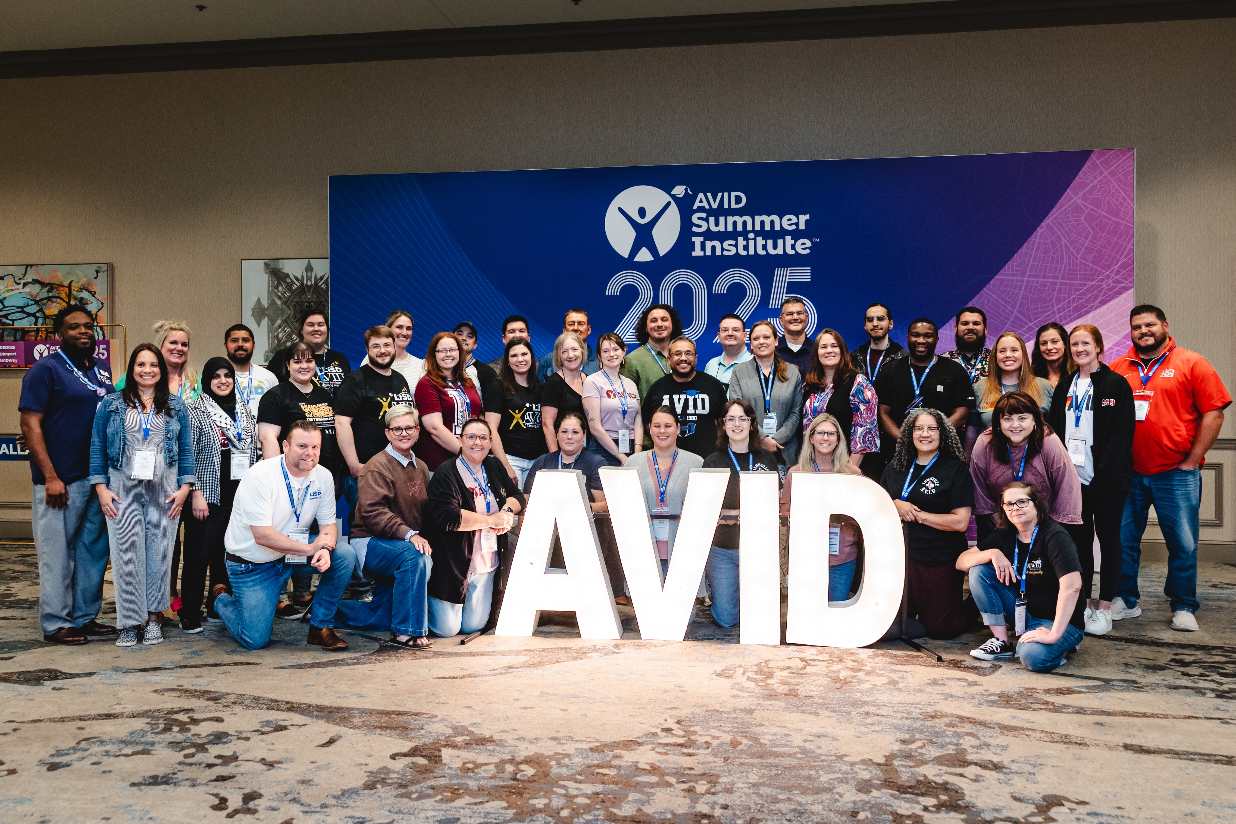 Group photo of individuals attending the AVID Summer Institute 2025, posed in front of a large AVID sign.