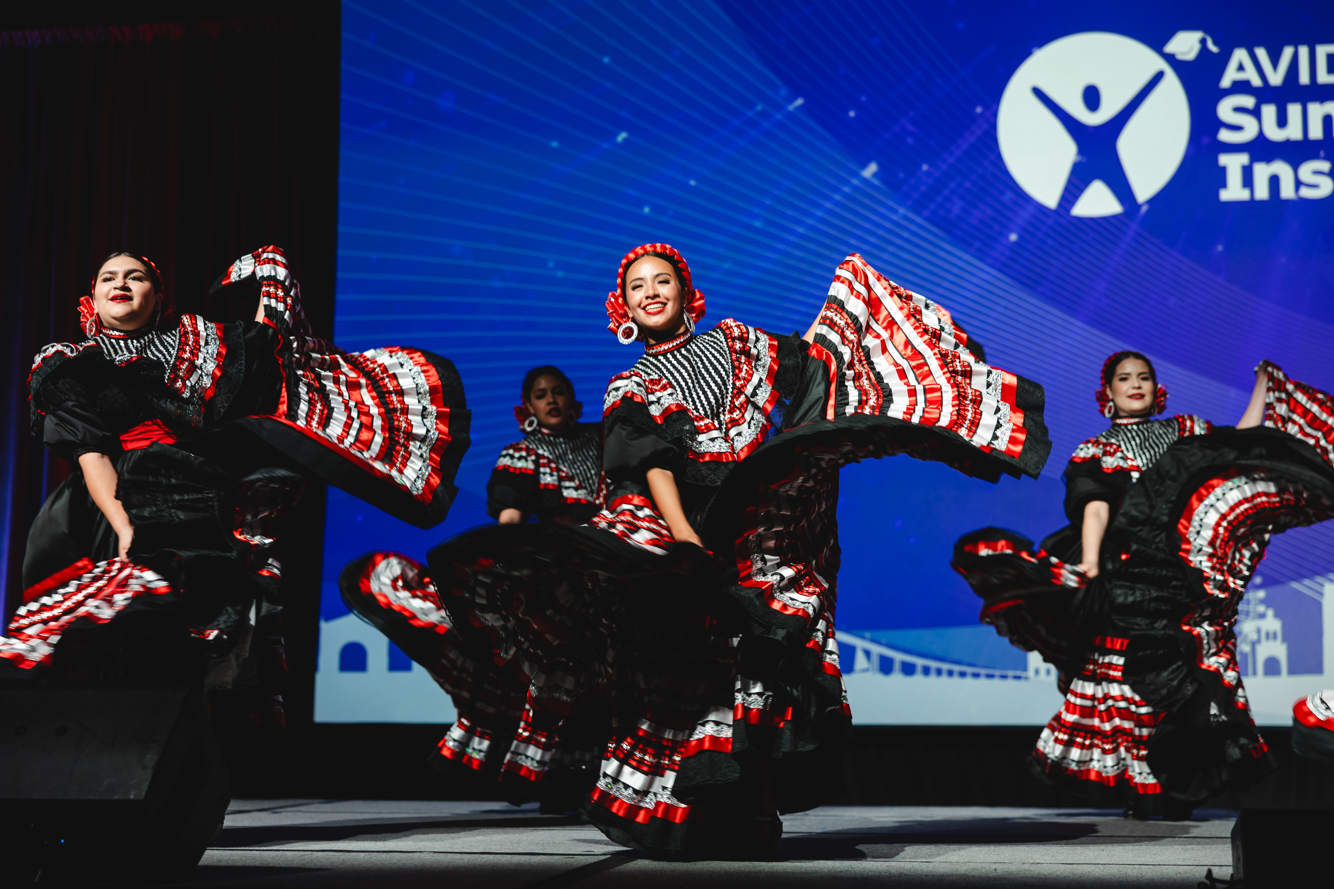 A group of dancers in colorful traditional outfits performing on stage at an event.