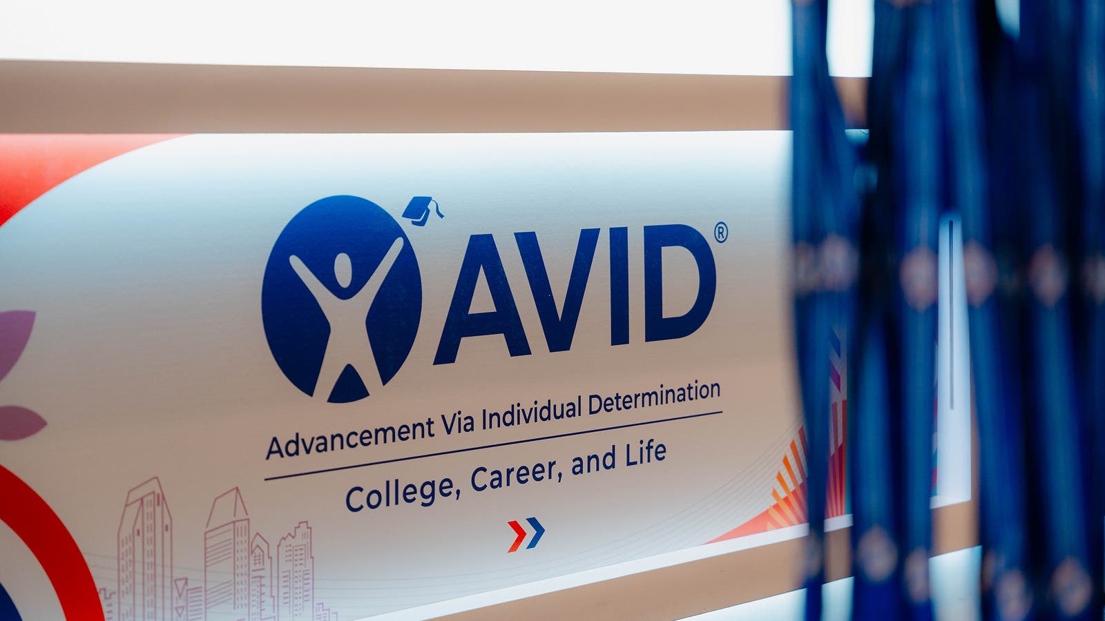 A banner displaying the AVID logo, which stands for Advancement Via Individual Determination, with the text 'College, Career, and Life.' The logo includes a silhouetted figure with arms raised inside a blue circle.