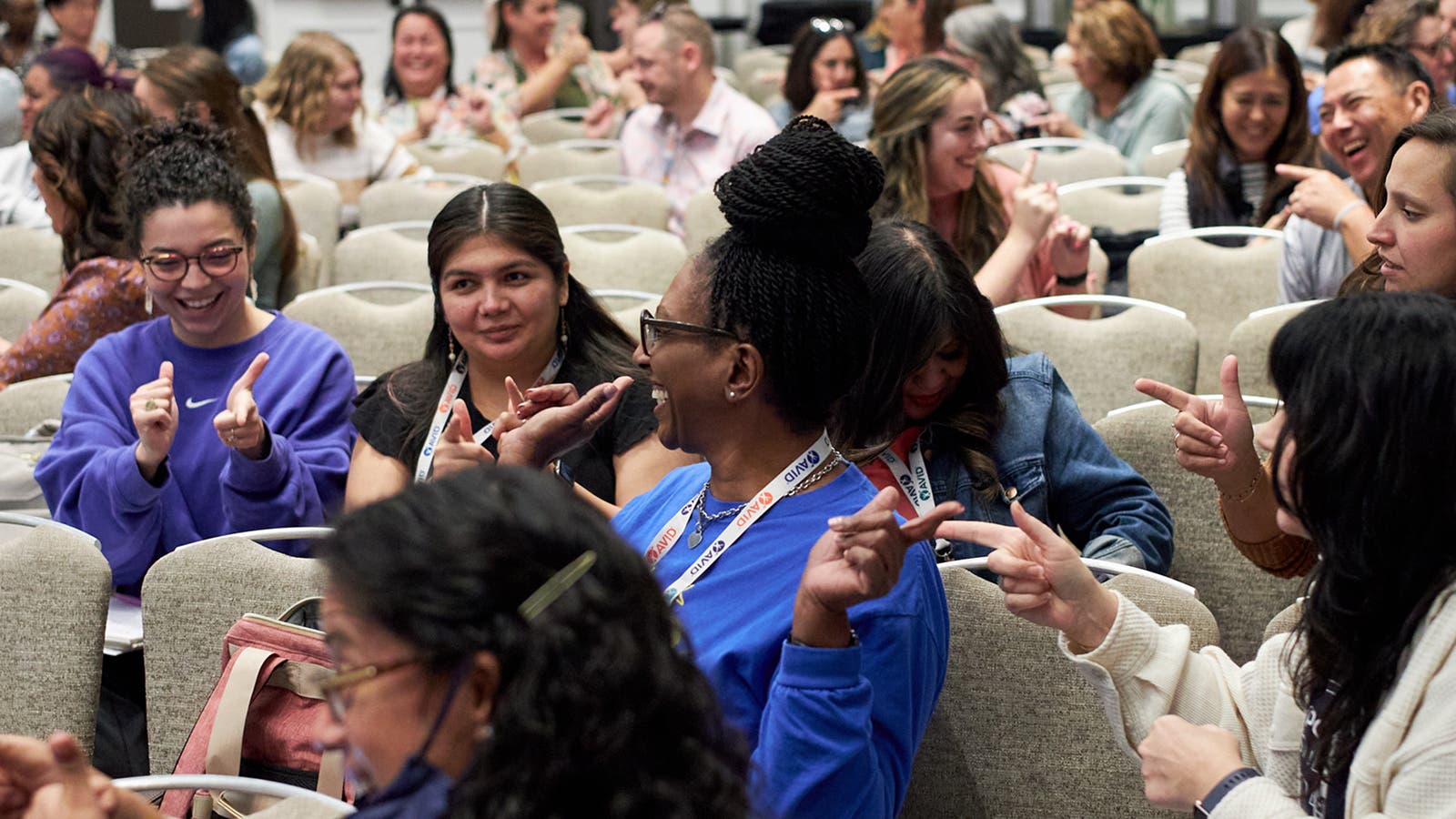 Group of people seated in chairs, engaged in a discussion while gesturing with their hands in a conference setting.