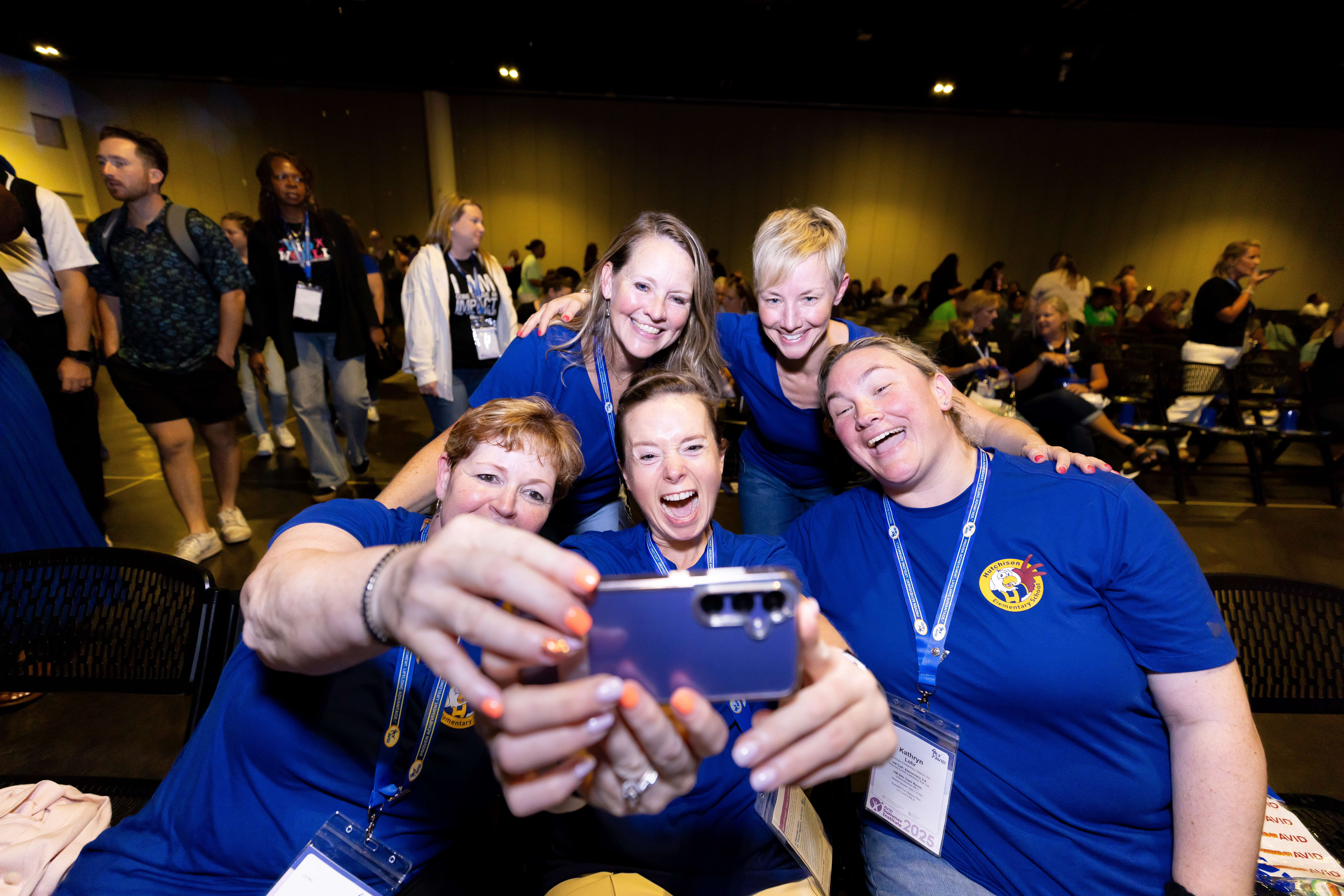 Group of people taking a selfie at an indoor event, wearing blue shirts and name tags.