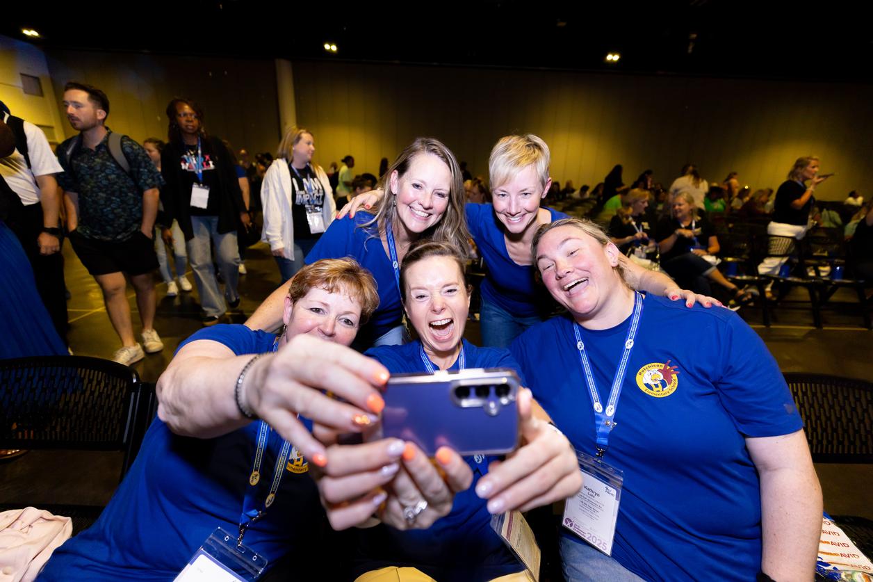 Group of people taking a selfie at an indoor event, wearing blue shirts and name tags. Group of people taking a selfie at an indoor event, wearing blue shirts and name tags.
