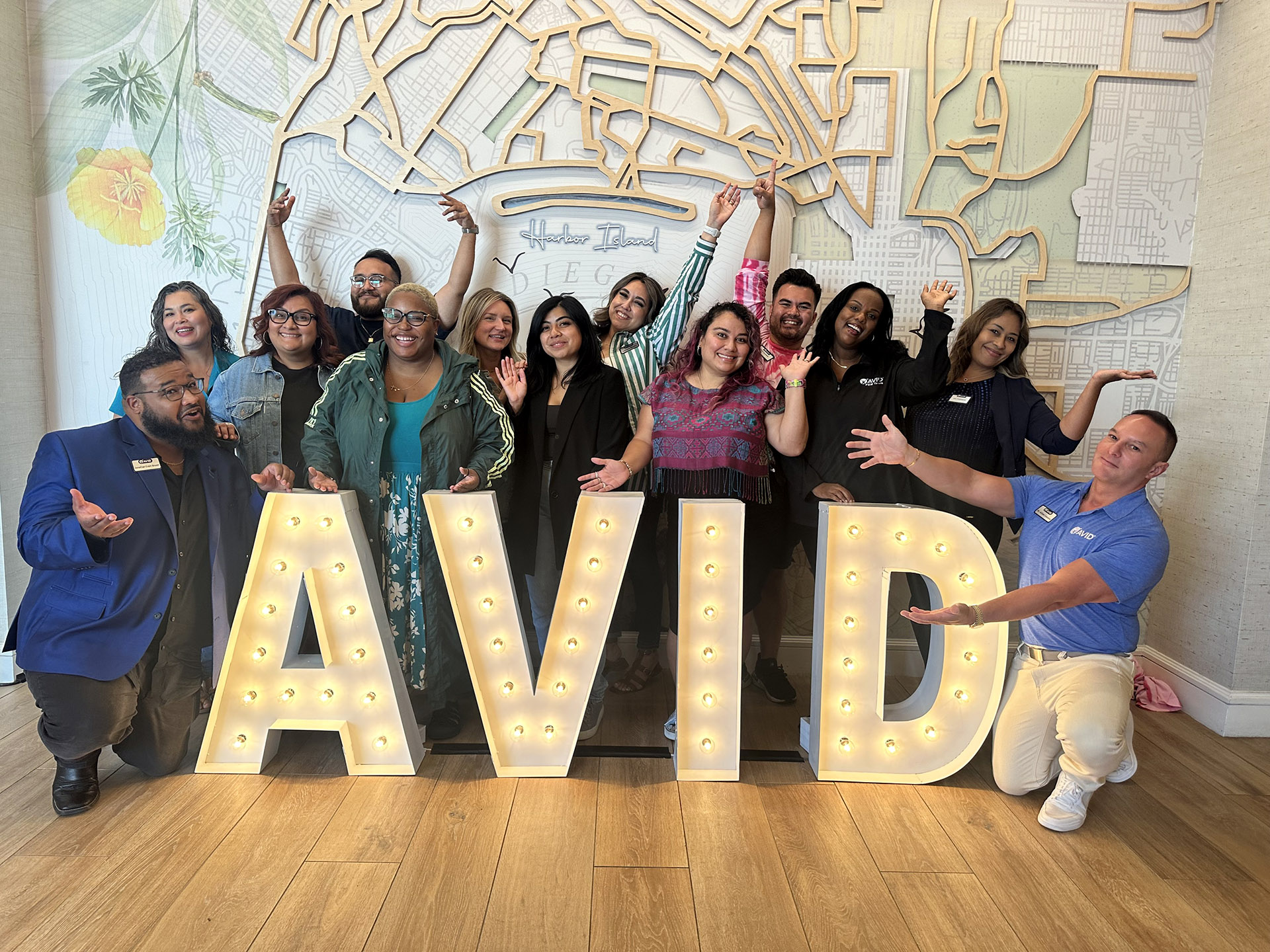 Group of people posing with large illuminated AVID letters in front of a map-themed background.