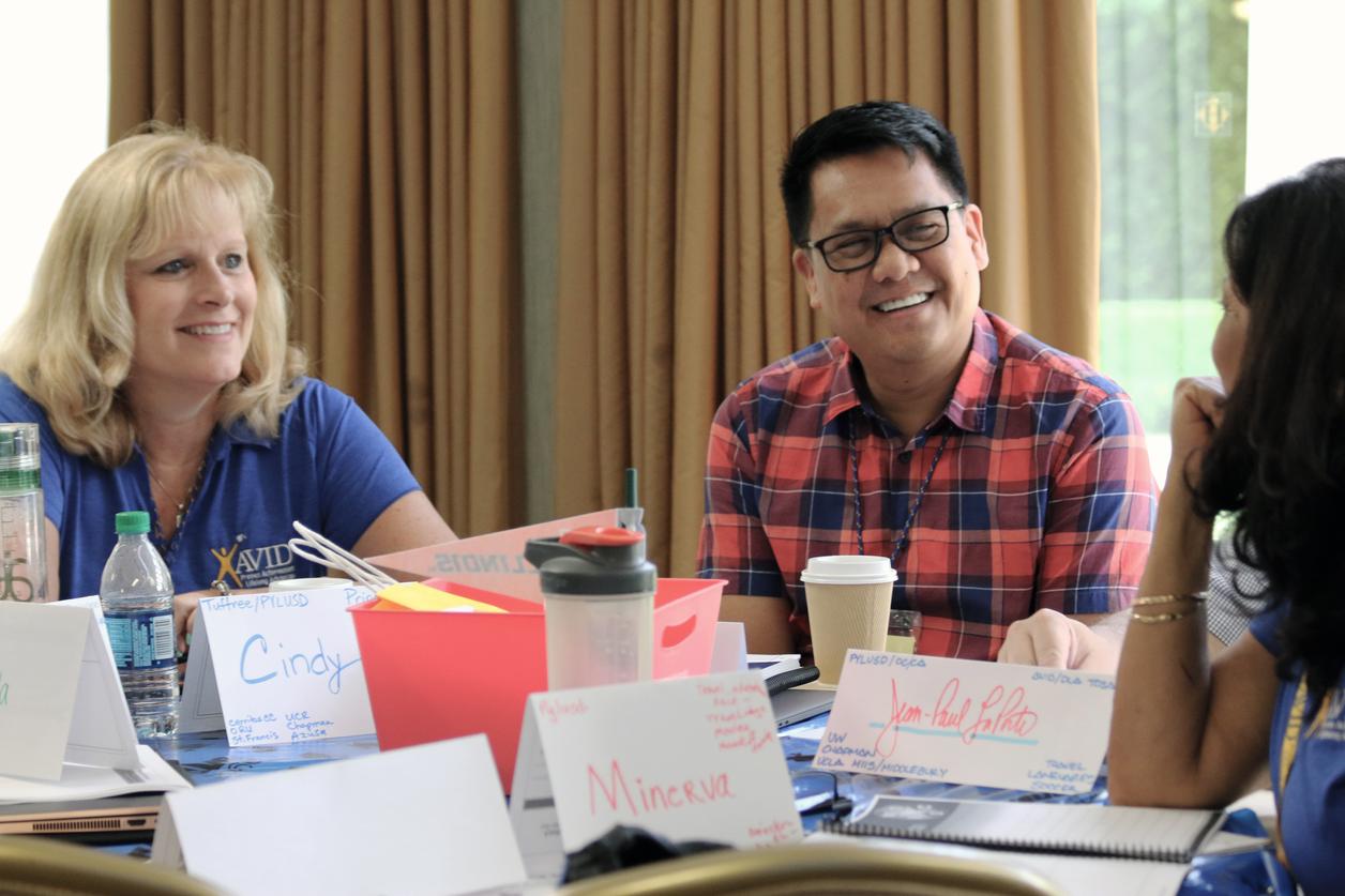 Group of people sitting around a table with name tags and water bottles in a meeting room. Group of people sitting around a table with name tags and water bottles in a meeting room.