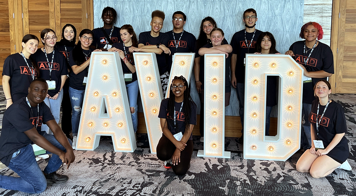 A group of people posing with large illuminated letters spelling out 'AVID' indoors.