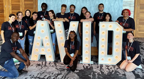 A group of people posing with large illuminated letters spelling out 'AVID' indoors. A group of people posing with large illuminated letters spelling out 'AVID' indoors.