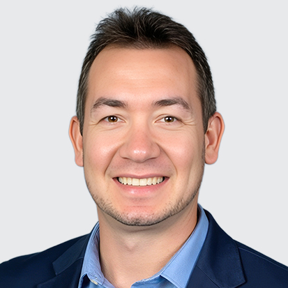 A photo of a person wearing a dark jacket and a light blue collared shirt against a plain background.