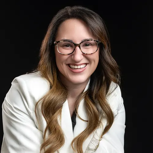 Individual with long, wavy hair wearing a white jacket against a black background, face blurred for anonymity. Individual with long, wavy hair wearing a white jacket against a black background, face blurred for anonymity.