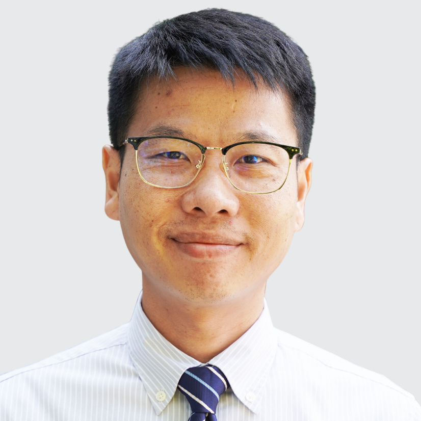 A person with short dark hair wearing glasses, a white shirt, and a striped tie, against a light gray background.