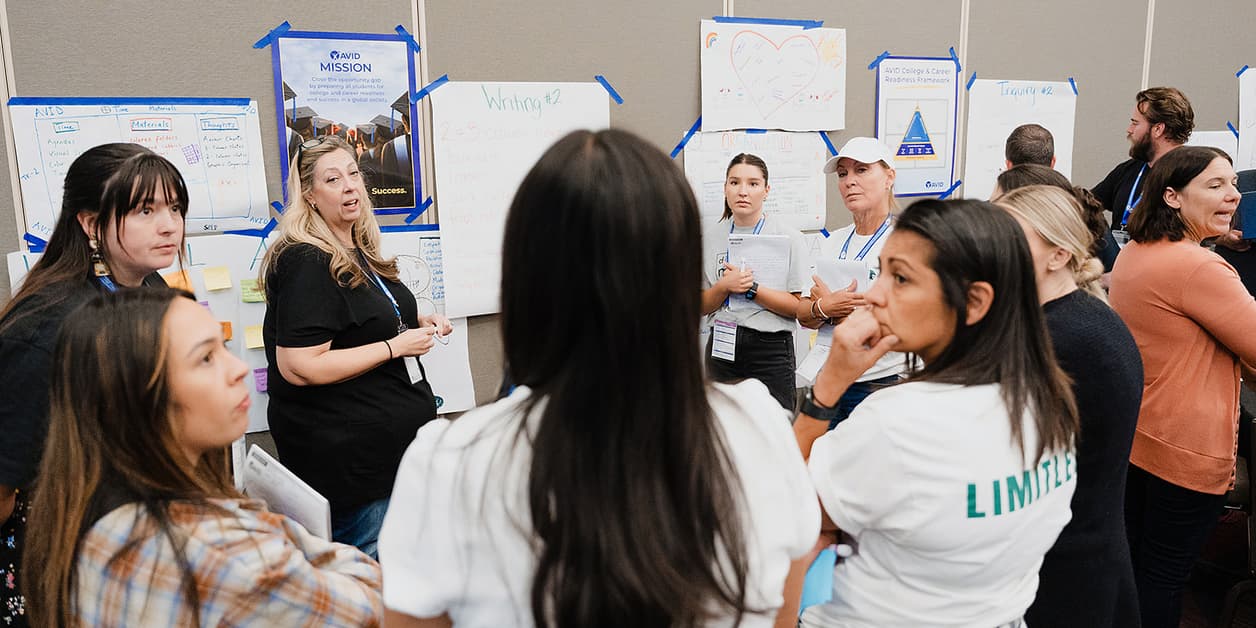 Group of people engaged in a workshop or discussion, standing near posters and whiteboards with various texts and diagrams. Group of people engaged in a workshop or discussion, standing near posters and whiteboards with various texts and diagrams.