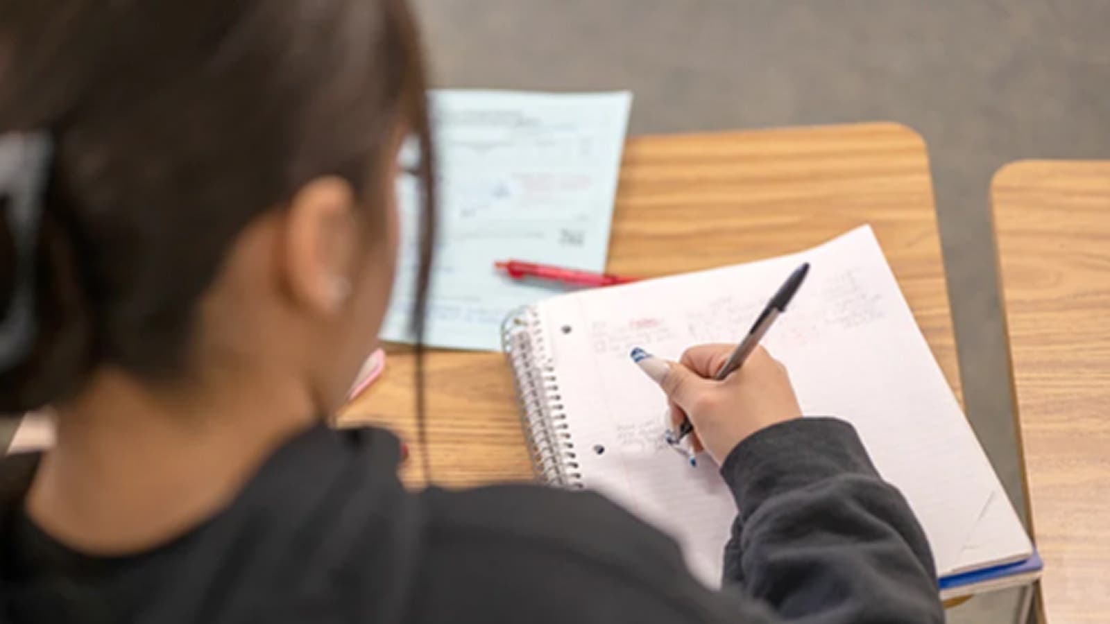 Person sitting at a table, writing in a notebook.