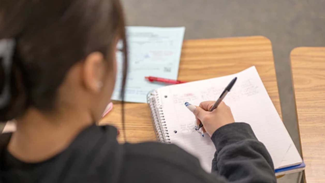 Person sitting at a table, writing in a notebook. Person sitting at a table, writing in a notebook.
