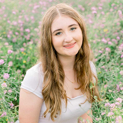 Person with long, wavy hair standing in a field of pink and purple flowers.