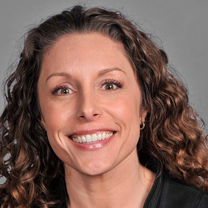 A person with curly hair wearing a black jacket against a gray background.