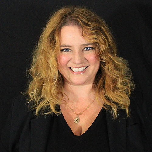 Individual with curly hair wearing a necklace and a dark top against a black background.