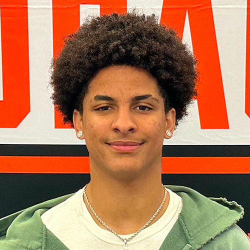 An individual with curly hair standing in front of a background with red and white text.