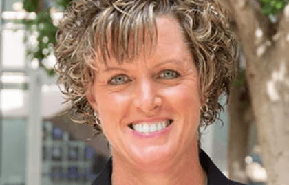 Person with curly hair standing in front of a blurred outdoor background with trees. Person with curly hair standing in front of a blurred outdoor background with trees.