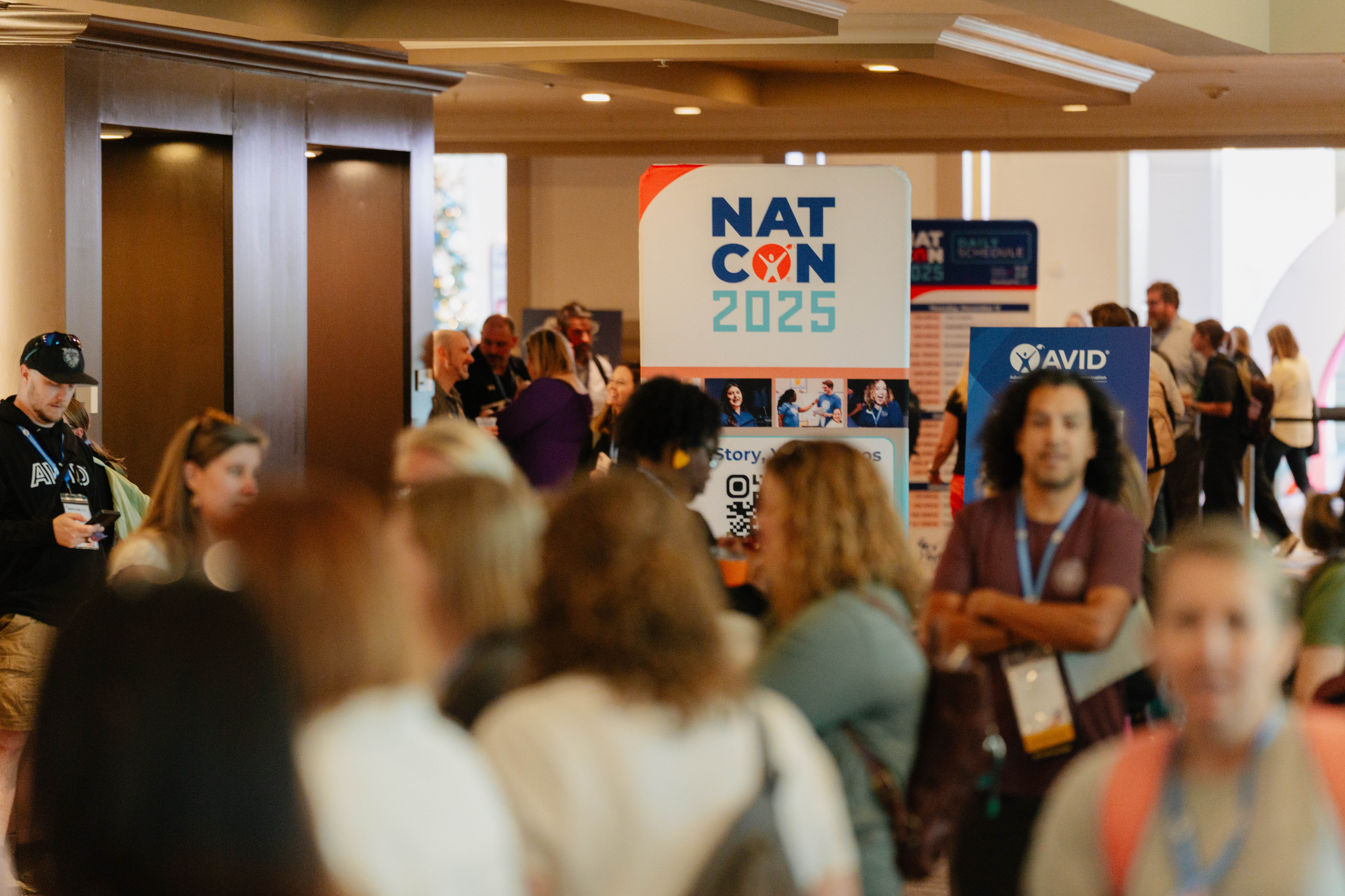 A large group of people at a conference with a sign displaying 'NATCON 2025' in the background.