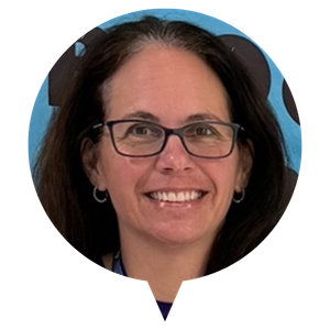 A person wearing glasses with long hair, smiling in front of a blue background.