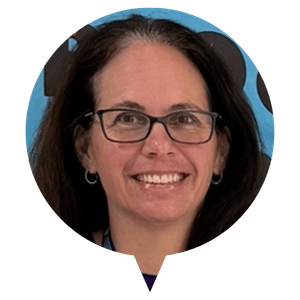 A person wearing glasses with long hair, smiling in front of a blue background. A person wearing glasses with long hair, smiling in front of a blue background.