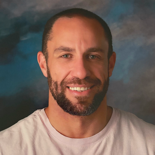 Person with face blurred, wearing a light-colored shirt against a cloudy background.