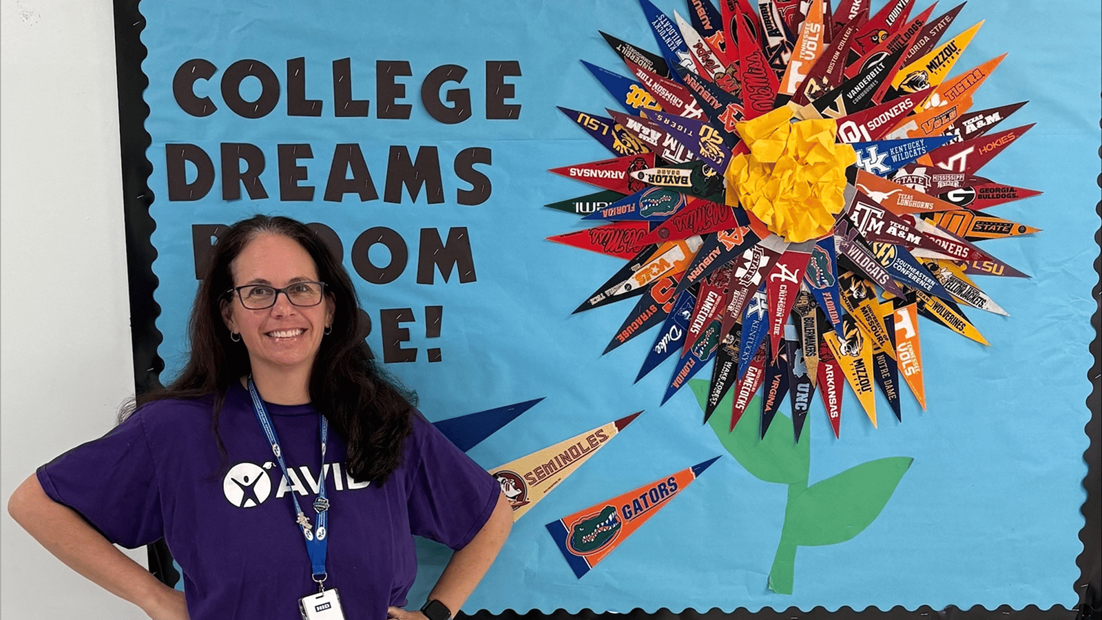 Person standing in front of a colorful bulletin board decorated with college pennants arranged like a flower and text saying 'College dreams bloom here.'