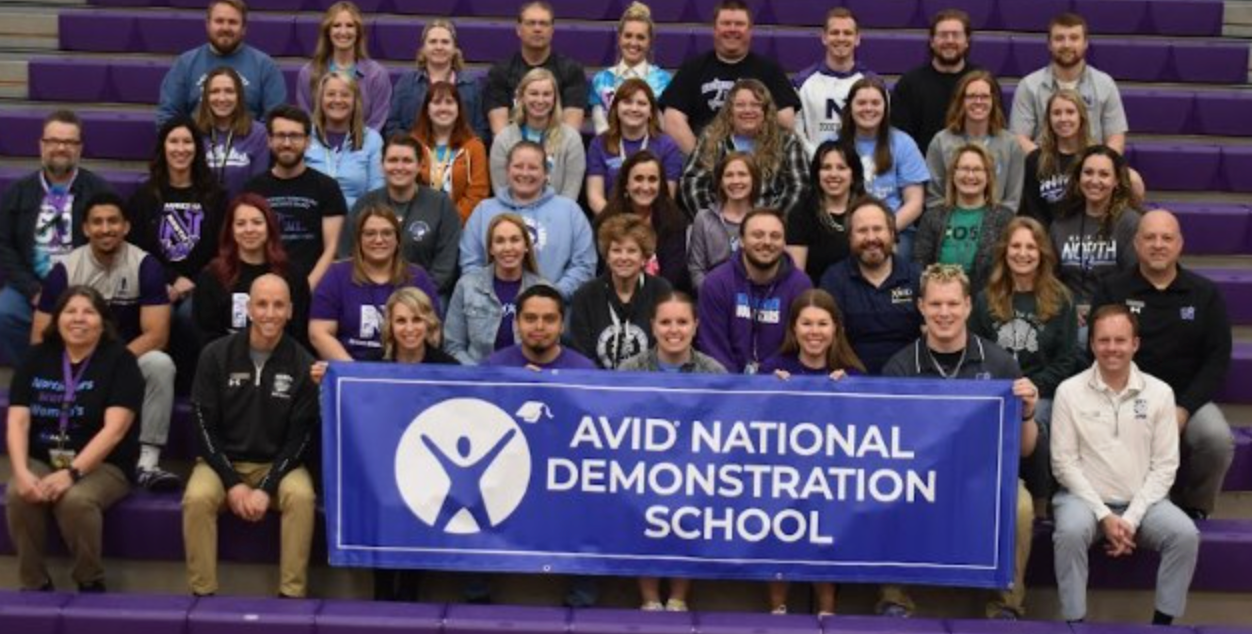 Group photo of people sitting on bleachers holding a banner that reads 'AVID National Demonstration School'.