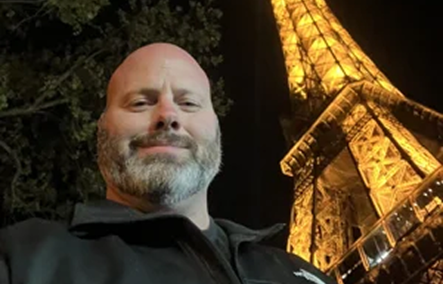 A person in a dark jacket standing in front of the illuminated Eiffel Tower at night.