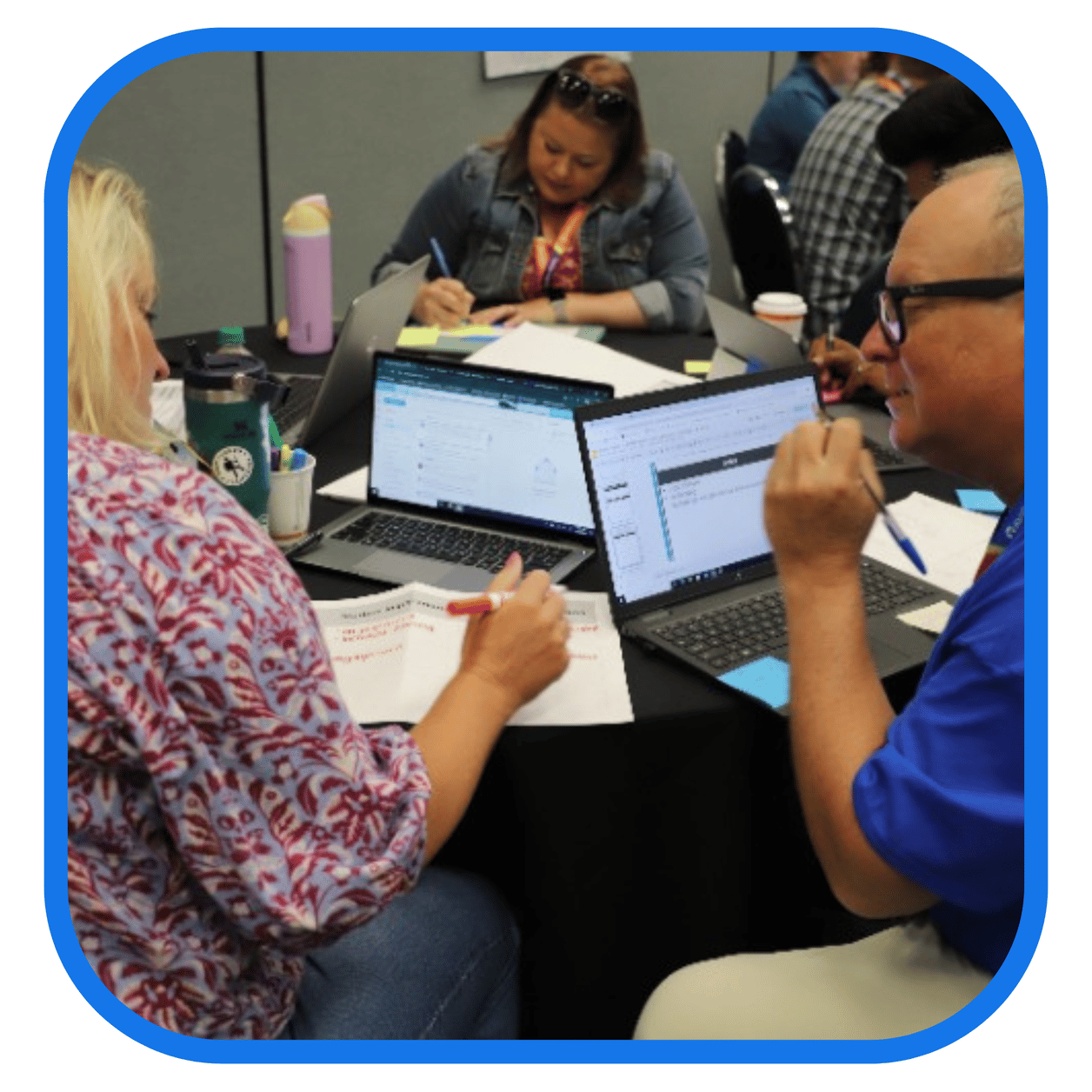 A group of people in a meeting or collaborative work setting, each with a laptop, writing on papers and discussing. A group of people in a meeting or collaborative work setting, each with a laptop, writing on papers and discussing.