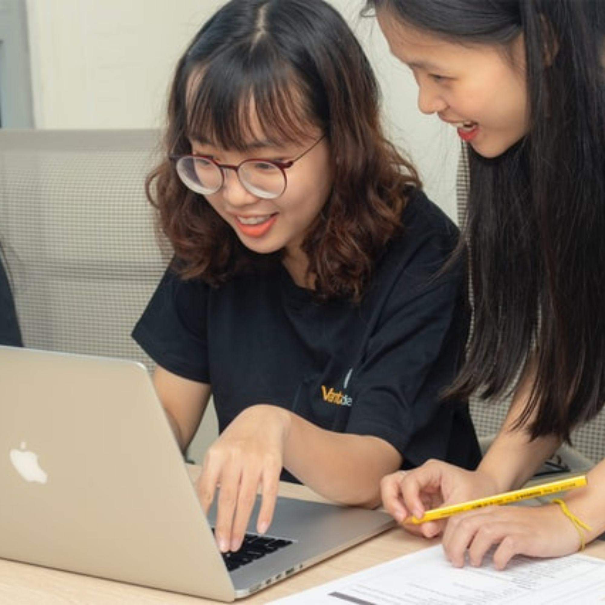 Two individuals collaborating on a laptop, one pointing at the screen with a pencil.