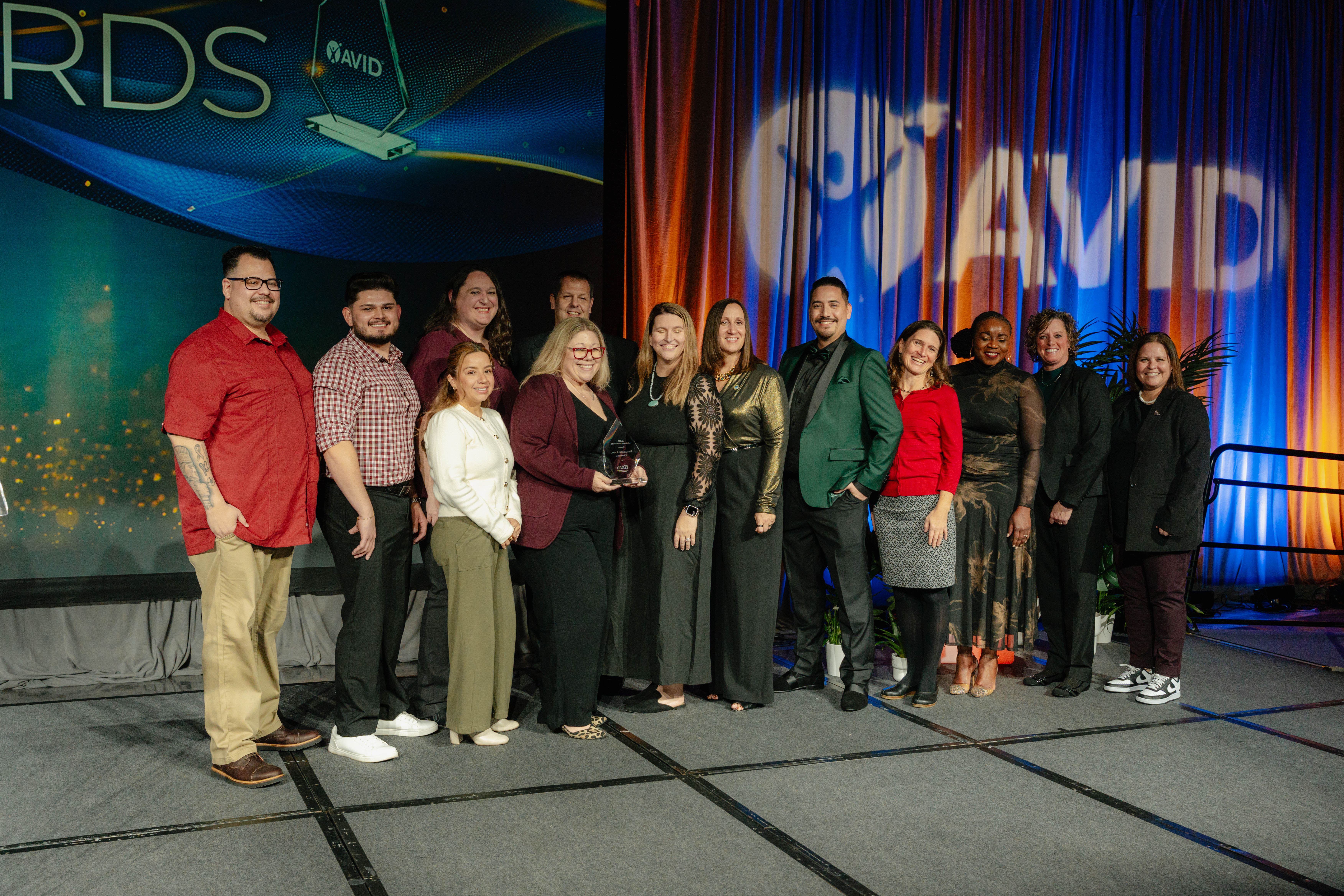 A group of people standing and posing with an award on a stage with an AVID logo and colorful backdrop.