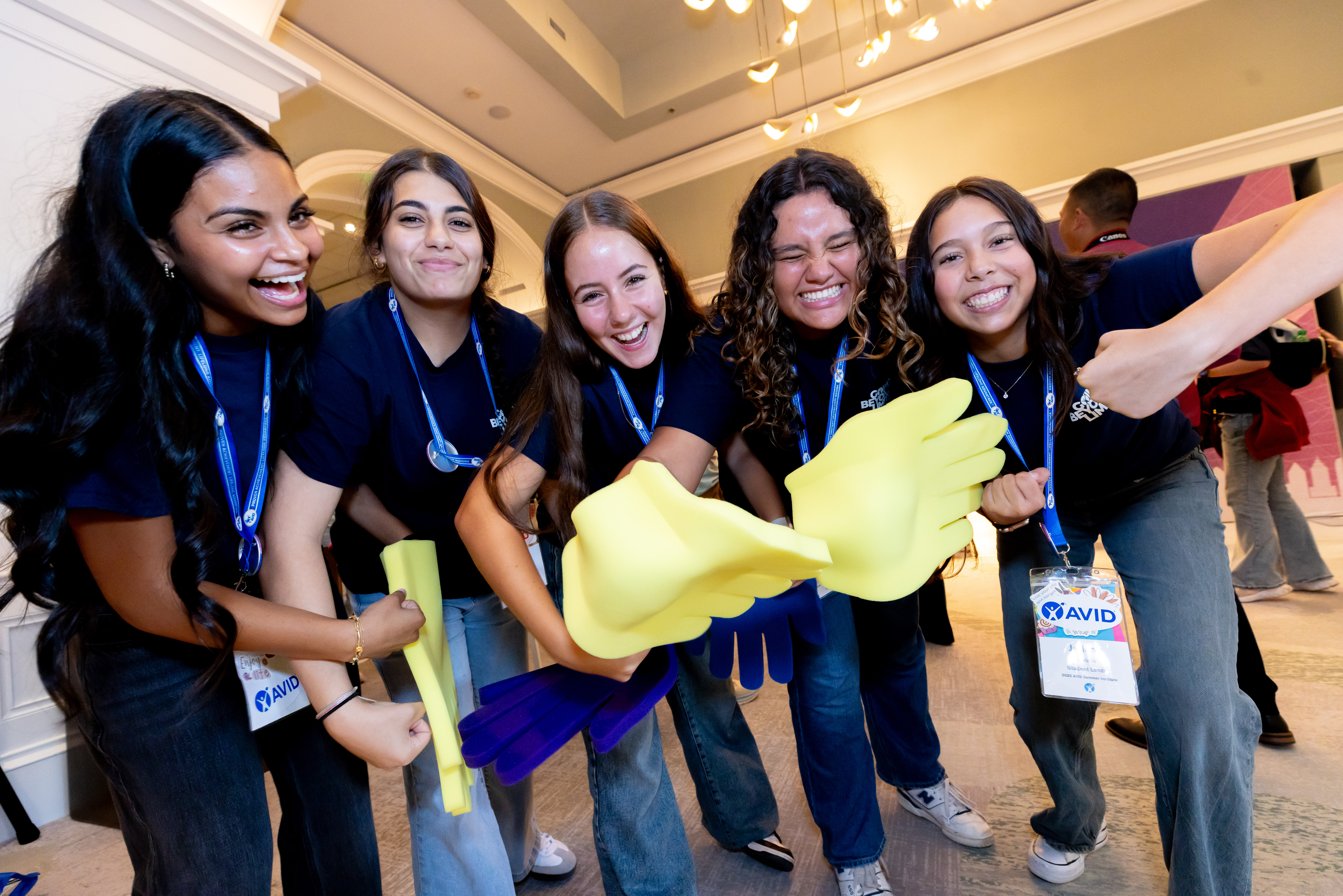 Group of people wearing lanyards and navy shirts, holding yellow and purple foam hands.