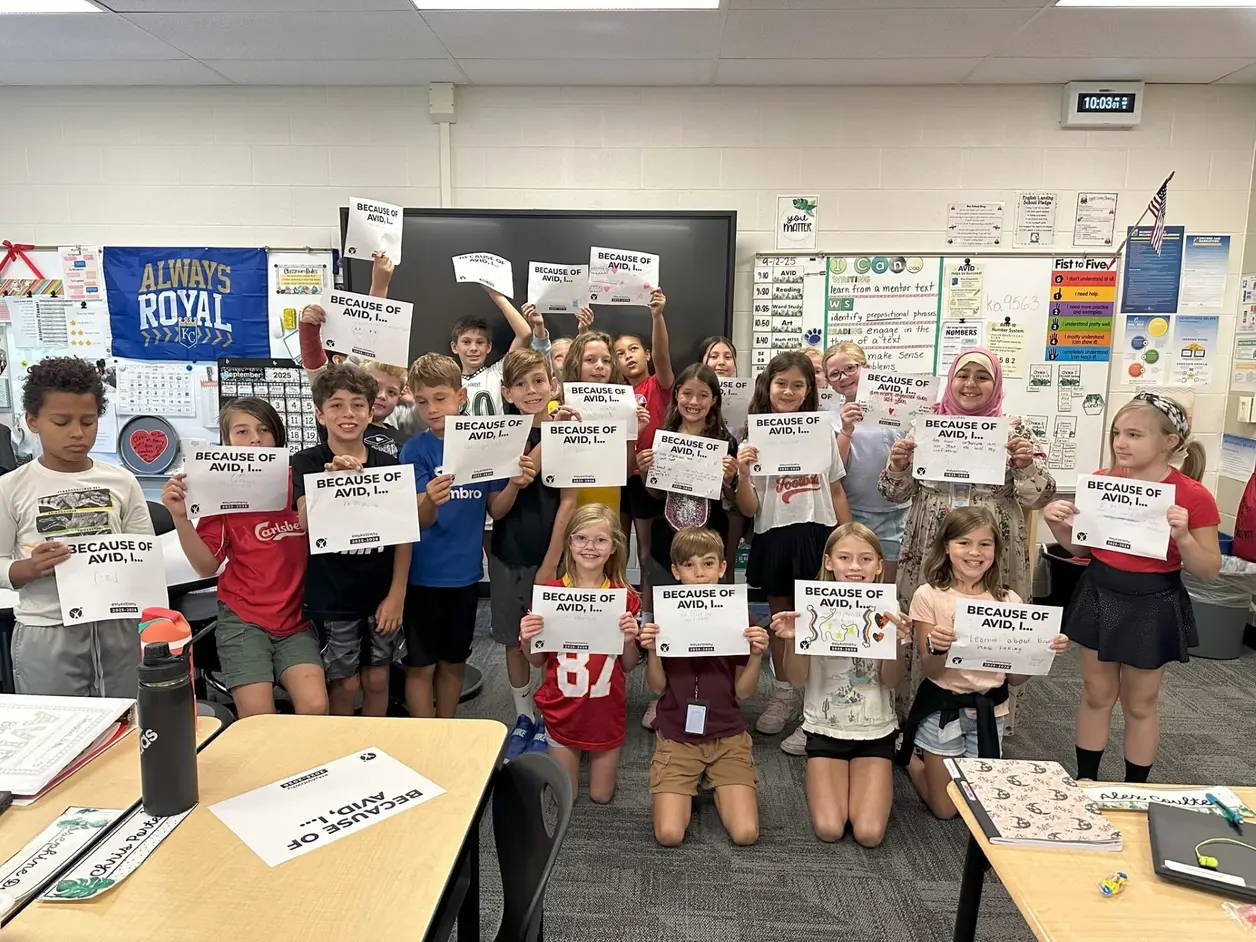 A group of students in a classroom holding signs that say 'BECAUSE OF AVID, I...' with educational posters and a 'Always Royal' banner in the background. A group of students in a classroom holding signs that say 'BECAUSE OF AVID, I...' with educational posters and a 'Always Royal' banner in the background.