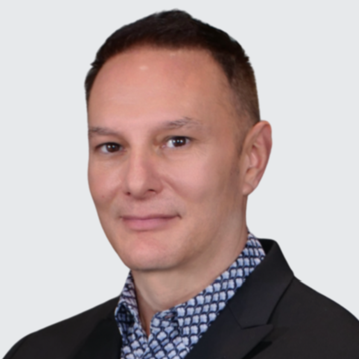 A person wearing a dark blazer over a patterned shirt, with their face blurred.